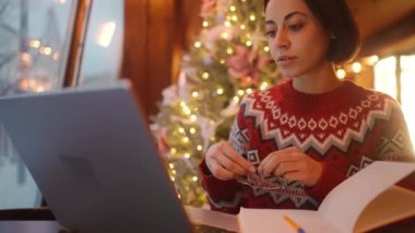 Noel arifesinde Xmass dekore edilmiş kahve dükkanında dizüstü bilgisayar ve defter kullanarak çalışan aşırı çalışan serbest çalışan bir kadın. Uzak çalışma serbest, proje bitiş tarihi, her şeyi yapmak