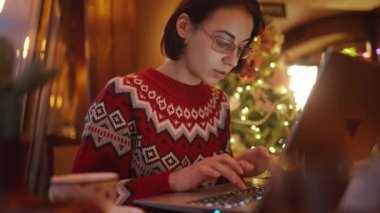 Noel arifesinde Xmass dekore edilmiş kahve dükkanında çalışan ve dizüstü bilgisayar, not defteri, fazla çalışma ve tatil konsepti kullanan stresli bir kadın. Uzak çalışma serbest, proje bitiş tarihi, her şeyi yapmak