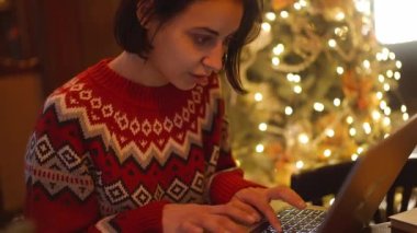 festive weared woman working in decorated cafe on Christmas Eve using laptop, typing. overwork and holidays concept. remote work freelancer, project deadline, do everything