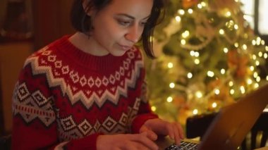 festive weared woman working in decorated cafe on Christmas Eve using laptop, typing. overwork and holidays concept. remote work freelancer, project deadline, do everything
