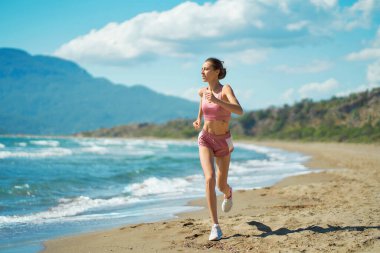 Athletic active runner jogging outdoors on beautiful tropical seashore with mountains view. Running woman healthy lifestyle