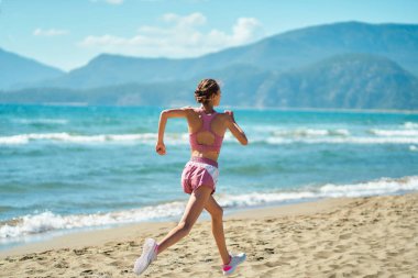 Back view active fitness runner female jogging outdoors on seashore with beautiful nature view. Sportswoman. Cardio exercises. Workout concept