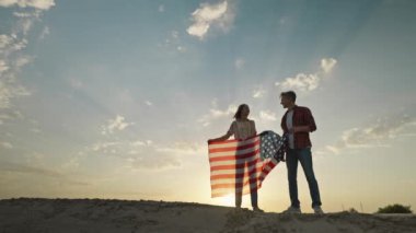 couple silhouette with flowing USA flag against sunset sky. 4th of july celebration outdoor, slow motion rural scene