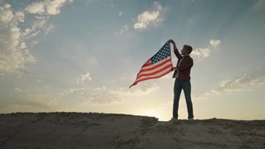 man silhouette with flowing USA flag against sunset sky. 4th of july celebration outdoor, slow motion rural scene