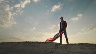 man silhouette with flowing USA flag against sunset sky. 4th of july celebration outdoor, slow motion rural scene