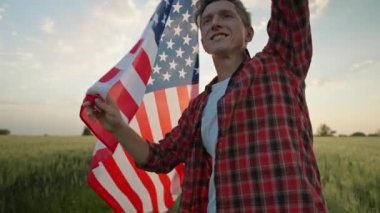 men energetically raised the US flag in a picturesque wheat field. farmer in a plaid shirt and jeans walks through field at sunset n and holds the American flag proudly over his head