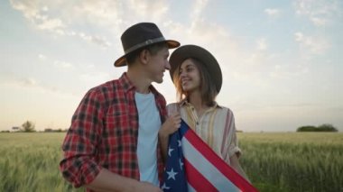 4k slow motion of happy patriotic couple celebrating fourth of july with national flag in rural lardmark at sunset. Federal holiday. 4 July Independence day celebrating with national American flag