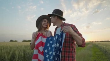 4k slow motion of happy patriotic couple celebrating fourth of july with national flag in rural lardmark at sunset. Federal holiday. 4 July Independence day celebrating with national American flag