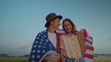 4k slow motion of happy patriotic couple celebrating fourth of july with national flag in rural lardmark at sunset. Federal holiday. 4 July Independence day celebrating with national American flag