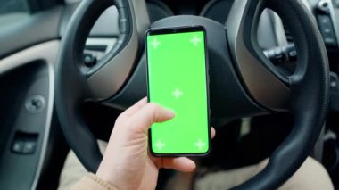 POV man in car at driver place, holds a phone with green screen with marks in hand. driver holds phone against steering wheel, swiping by finger in different directions. navigation, shopping concept