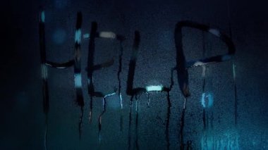 a word Help written with a finger on the misted glass against lights at night. water drops flow down the glass. plea for help, danger signal, hostage taking, domestic violence