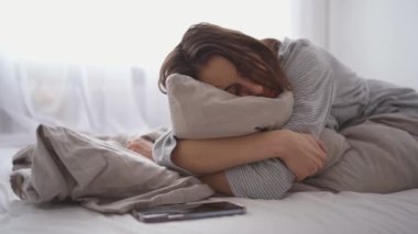 young woman lies alone on bed at home, cold and sick. illness, cold, virus, doctors call at home, consultation with a doctor by phone