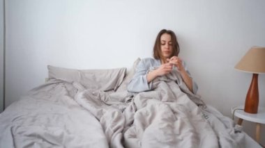 young woman lies alone on bed at home, cold and sick. illness, cold, virus, doctors call at home, consultation with a doctor by phone