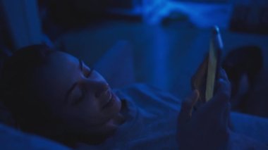night scene. woman lying in dark room on coach with phone in hands. girl textin and messaging at night in chats or social networks alone at home