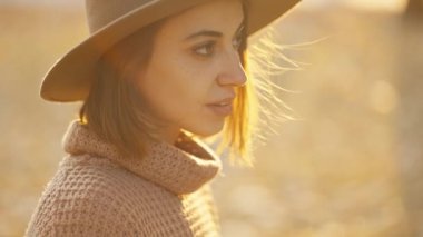 close up autumn portrait of beautiful smiling woman wearing in wrown dress, sweater and hat. girl holds yellow leaves and playfuly looking at camera