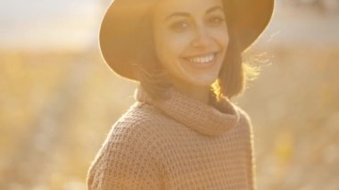 close up autumn portrait of beautiful smiling woman wearing in wrown dress, sweater and hat. girl holds yellow leaves and playfuly looking at camera