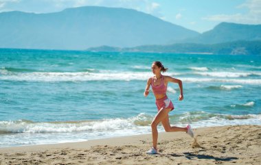 Healthy sportive wellbeing woman running along beautiful seashore. Morning workout training outdoors