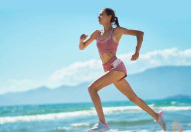 Athletic female sprinting, running fast, exercising cardio workout outdoors at sunny beach. Strong healthy body woman