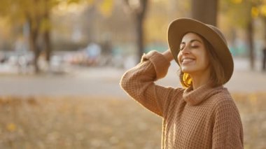 close up portrait of stunning young brunette woman in autumn forest with yellow foliage against sunset sun with sunflare. stylish attractive girl walks in park at warm fall day. slow motion 4k footage