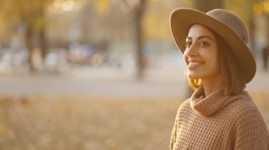 close up portrait of stunning young brunette woman in autumn forest with yellow foliage against sunset sun with sunflare. stylish attractive girl walks in park at warm fall day. slow motion 4k footage
