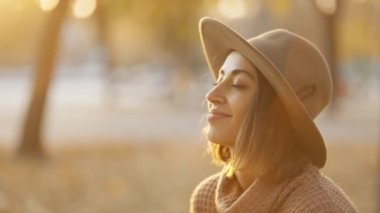 close up portrait of stunning young brunette woman in autumn forest with yellow foliage against sunset sun with sunflare. stylish attractive girl walks in park at warm fall day. slow motion 4k footage