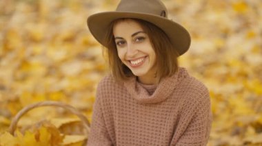 slow motion portrait of charming happy brunette woman at picnic in bright autumn park with yellow foliage. stylish attractive girl sits on blanket in park at warm fall day and drinks coffee.