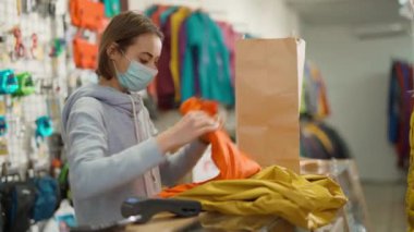 woman seller behind counter of outdoors store receives selected product from buyer and packs it. season sale, new collection in clothing and equipment store for sports and outdoor activities