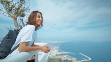 Sırt çantalı neşeli turist kadın dağın tepesinde duruyor, Tunektepe Teleferik, Antalya manzarasının tadını çıkarıyor.