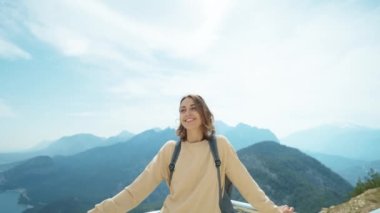 Positive smiling young caucasian woman tourist enjoying breathtaking view at viewpoint among mountains. Adventure and travel exploring