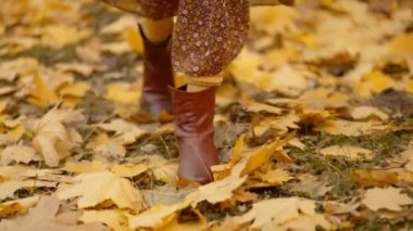 slow motion close up legs in leather boots of charming woman walks in bright autumn park with yellow foliage. stylish vintage woman in park at warm fall day