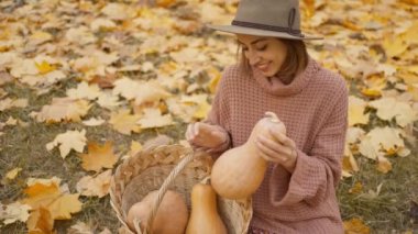 slow motion close up charming woman walks in bright autumn park with yellow foliage. stylish vintage woman in park at warm fall day holds wicker basket with orange pumpkins