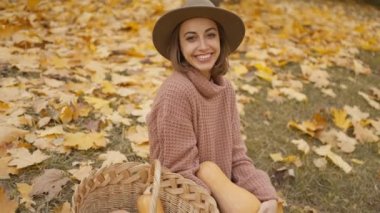 slow motion close up charming woman walks in bright autumn park with yellow foliage. stylish vintage woman in park at warm fall day holds wicker basket with orange pumpkins