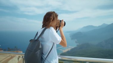 attractive woman hipster travel blogger takes photo on professional camera, viewpoint among mountains and blue sky, cableway destination. viewpoint of Tunektepe Teleferik, Antalya, Turkey