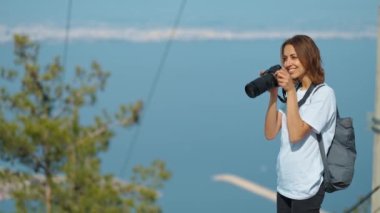 pretty woman travel blogger taking photo or video on professional camera, viewpoint among mountains and blue sky, cableway on background. viewpoint of Tunektepe Teleferik, Antalya, Turkey