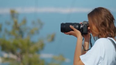 pretty woman travel blogger taking photo or video on professional camera, viewpoint among mountains and blue sky, cableway on background. viewpoint of Tunektepe Teleferik, Antalya, Turkey