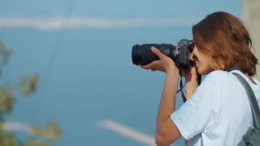 pretty woman travel blogger taking photo or video on professional camera, viewpoint among mountains and blue sky, cableway on background. viewpoint of Tunektepe Teleferik, Antalya, Turkey