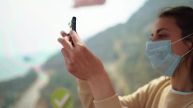 Yüzü maskeli genç bir turist teleferik içinde oturmuş kamerasıyla manzara çekiyordu. Antalya, Türkiye 'de kablo yolu