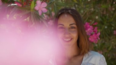 Yakından güzel bir portre. Siyah saçlı gülümseyen bir kız. Ağaçta duran pembe çiçeklere bakıyor..