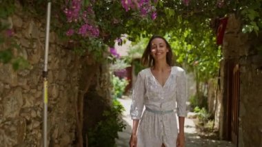 Ağır çekimde gülümseyen, kaygısız, beyaz elbiseli, çiçeklerle yürüyen güzel bir kadın, şehrin eski bölümünde Datcha, Türkiye 'de tatilin tadını çıkarıyor..