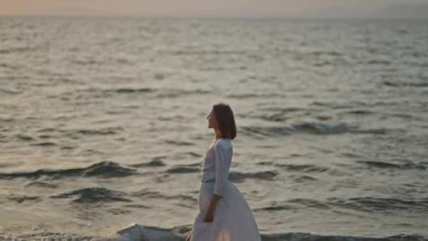 Kobieta Eleganckiej Długiej Białej Sukience Spaceruje Plaży Morskiej Podczas Pomarańczowego — Wideo stockowe