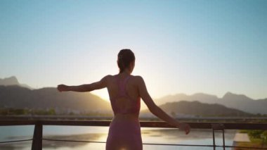 Silüet sağlıklı atletik kadın köprüde kolları açık ve esniyor. Isınma ve yoga güneşini doğa görüşüyle selamlama alıştırması.