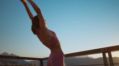 Vrksasana egzersizinde, ağaç duruşu ve spor yaparak yoga yapan genç bir kadın. Güzel karanlık gün batımı gökyüzü ve arka planda dağlar.