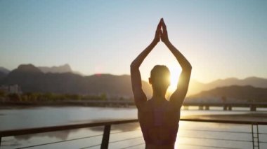 Vrksasana egzersizinde, ağaç duruşu ve spor yaparak yoga yapan genç bir kadın. Güzel karanlık gün batımı gökyüzü ve arka planda dağlar.