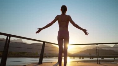 Arka manzara, siluet sportif kadın, elleri ağaç yogası pozunda köprüde duruyor. Gün batımında doğa manzaralı yoga pratiği yapmak.