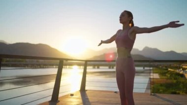 Gün batımında elleri havada bir kadın silueti. Yoga yapıyor ve dağ sırasına karşı köprüde meditasyon yapıyor.