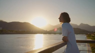 Kamera mutlu, tasasız genç bir kadının etrafında dönüyor. Köprü parmaklıklarında dikiliyor, turuncu gökyüzü ile günbatımının tadını çıkarıyor. Dağlar ve deniz manzaralı gün batımı manzarası
