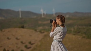 Beyaz elbiseli çekici bir kadın fotoğrafçı doğada güzel manzaralarda fotoğraf çekiyor.