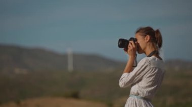 Beyaz elbiseli çekici bir kadın fotoğrafçı doğada güzel manzaralarda fotoğraf çekiyor.