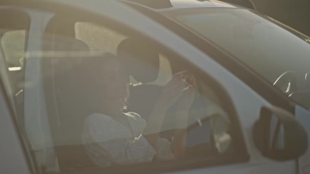 在野外旅行时 穿着浅白衣服坐在小木屋里的中弹美女 电话在车里等着的女人 透过玻璃窗拍摄 — 图库视频影像