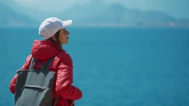 Türkiye 'nin Antalya kentinde, parlak kırmızı ceketli, kollarını açmış mutlu, genç bir kadın yolcunun arka görüntüsü. Turkuaz Akdeniz, koy ve dağ sırtı manzarası